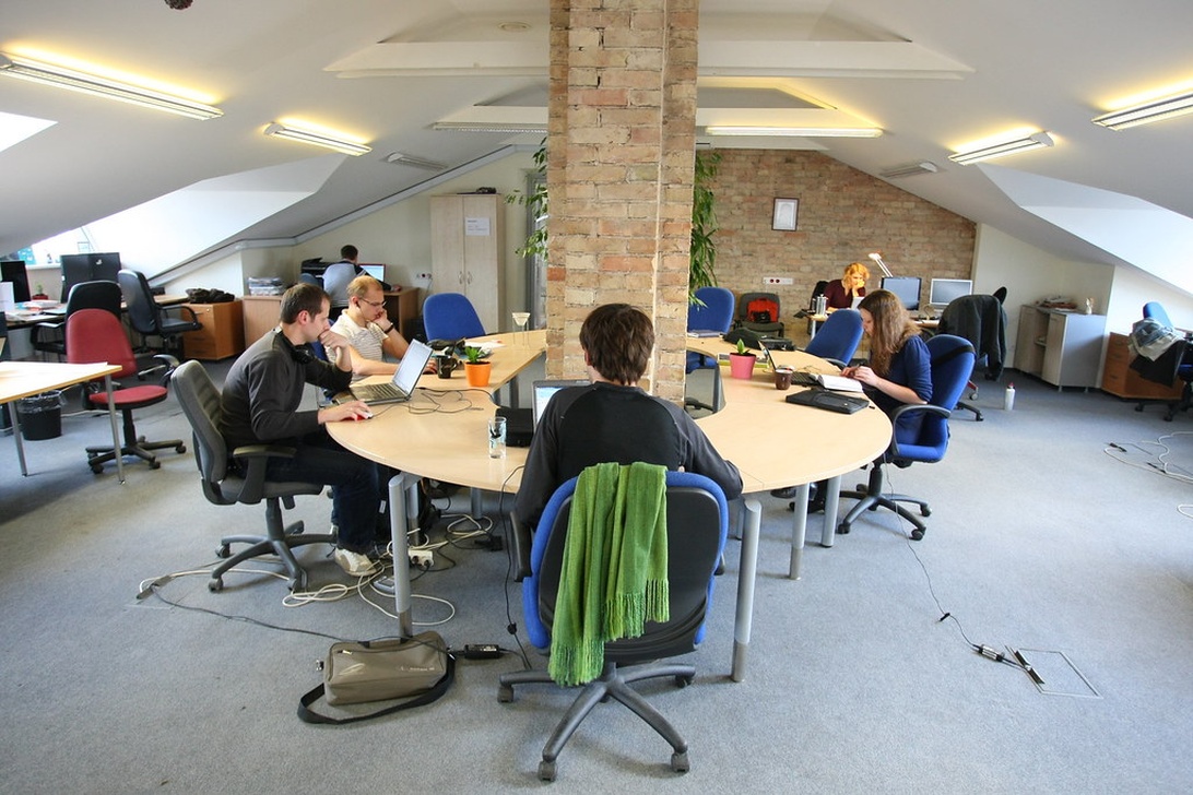 En ljus och öppen coworking-miljö med tegelpelare där flera personer arbetar vid ett stort, halvcirkelformat skrivbord.