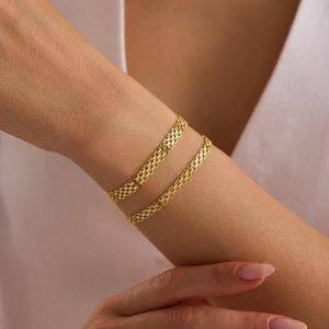 Två eleganta Bismarck armband i guld på en handled.