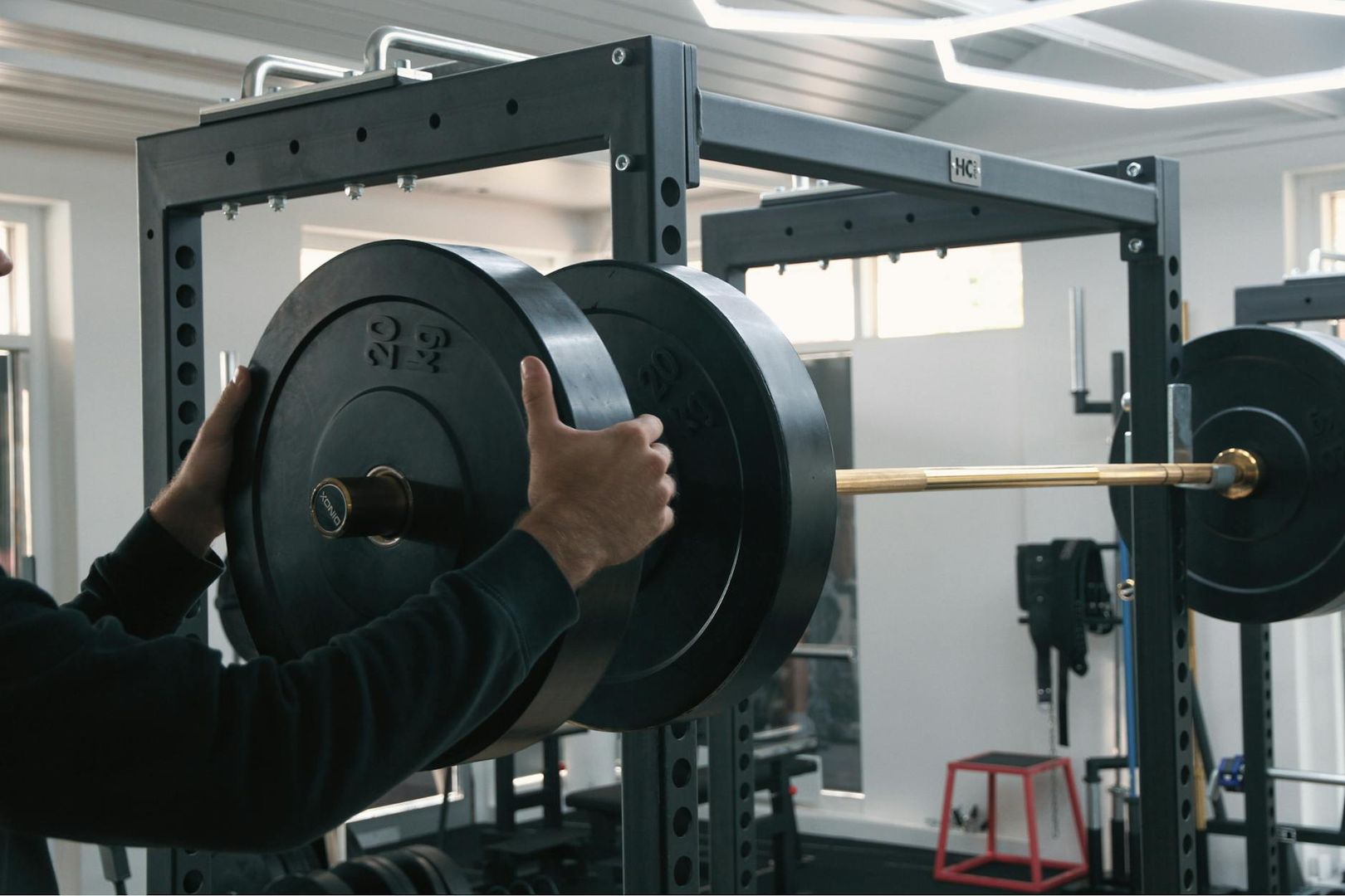 En person monterar tunga viktskivor på en skivstång i en squat rack.